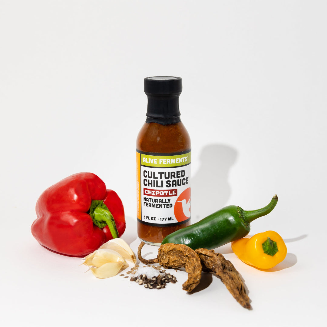 Bottle of cultured chili sauce with peppers and garlic on a white background
